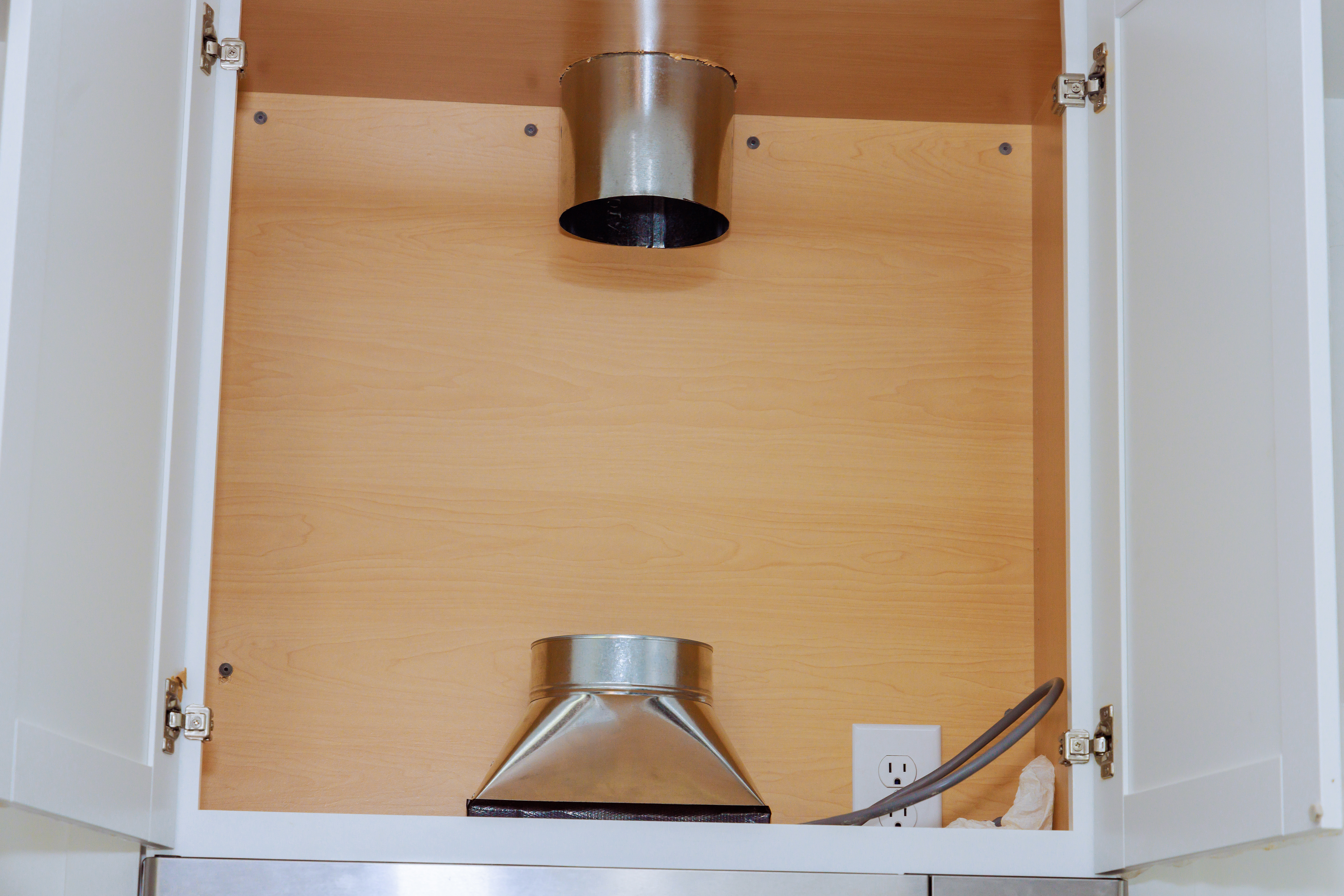 A close-up of rigid metal ducting installed inside a kitchen cabinet